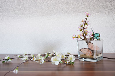 Close-up of ikebana with artificial butterflies on table against white wall