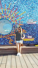 Young woman standing on boardwalk against mosaic wall