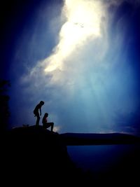 Silhouette people standing on rock against sky