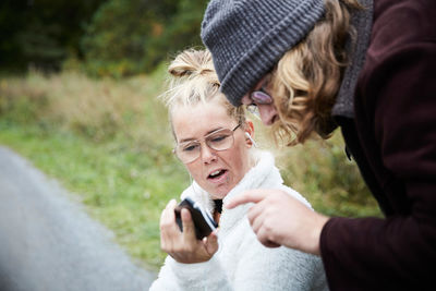 Young male caretaker and disabled woman using mobile phone outdoors