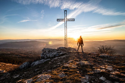 Man standing on rock against sky during sunset