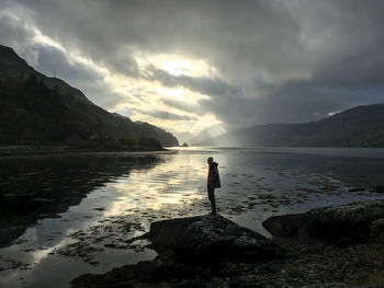 Rear view of woman standing on lake against sky