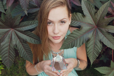 Portrait of young woman holding prism while standing against plant