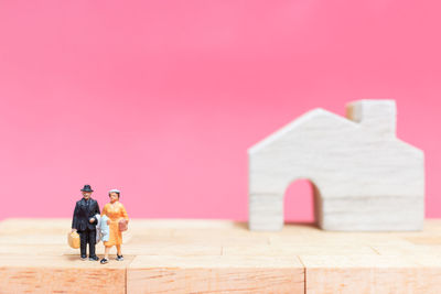 Close-up of figurines with model home on table against pink background