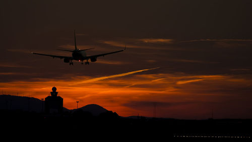 Silhouette airplane flying over control tower at budapest ferenc liszt international airport against sky