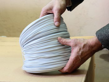 Cropped hands of man holding rolled up cable on table