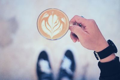 Low section of man holding coffee cup while standing on street