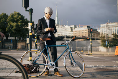 Businessman using mobile phone while standing by bicycle on street in city