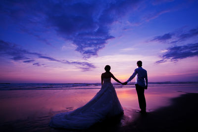 Bride and groom standing on shore during sunset