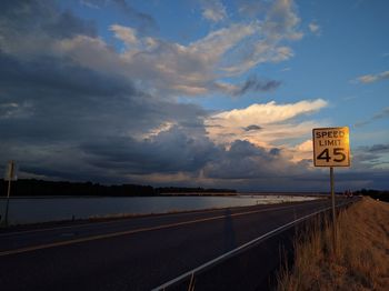 Road sign by sea against cloudy sky