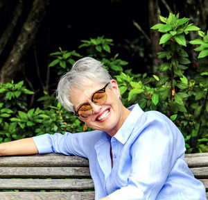 Portrait of smiling senior woman wearing sunglasses while sitting in park