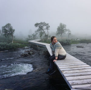 Young woman sitting on bridge over river