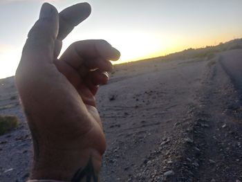 Close-up of hands on sand at beach against sky