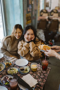 Happy female friends looking at food being served at restaurant