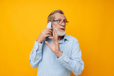 Young man talking on phone while standing against yellow background