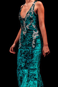 Details of a velvet green evening dress on a female figure on a black background.