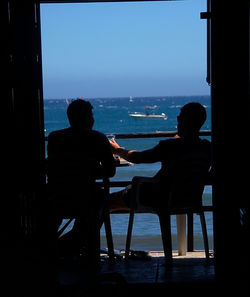 Rear view of silhouette people sitting on chair at beach