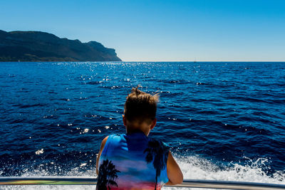 Rear view of man standing at beach against clear blue sky