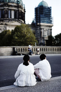 Rear view of couple sitting on sidewalk