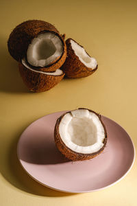 Coconut half in pink plate with nut fruits on cream yellow plain background