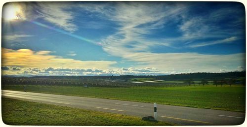 Road passing through field against cloudy sky