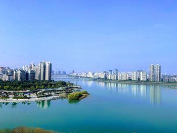 Scenic view of river by buildings against clear blue sky