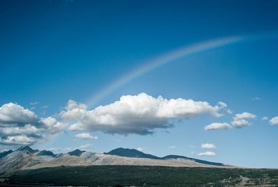 Scenic view of rainbow over landscape against blue sky