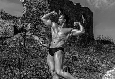 Shirtless man flexing muscles against old ruins on sunny day