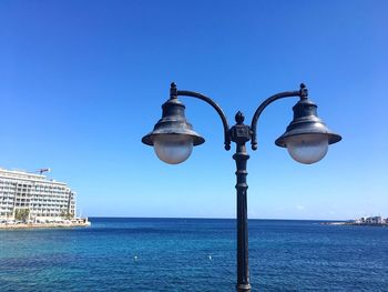 Street light by sea against clear blue sky