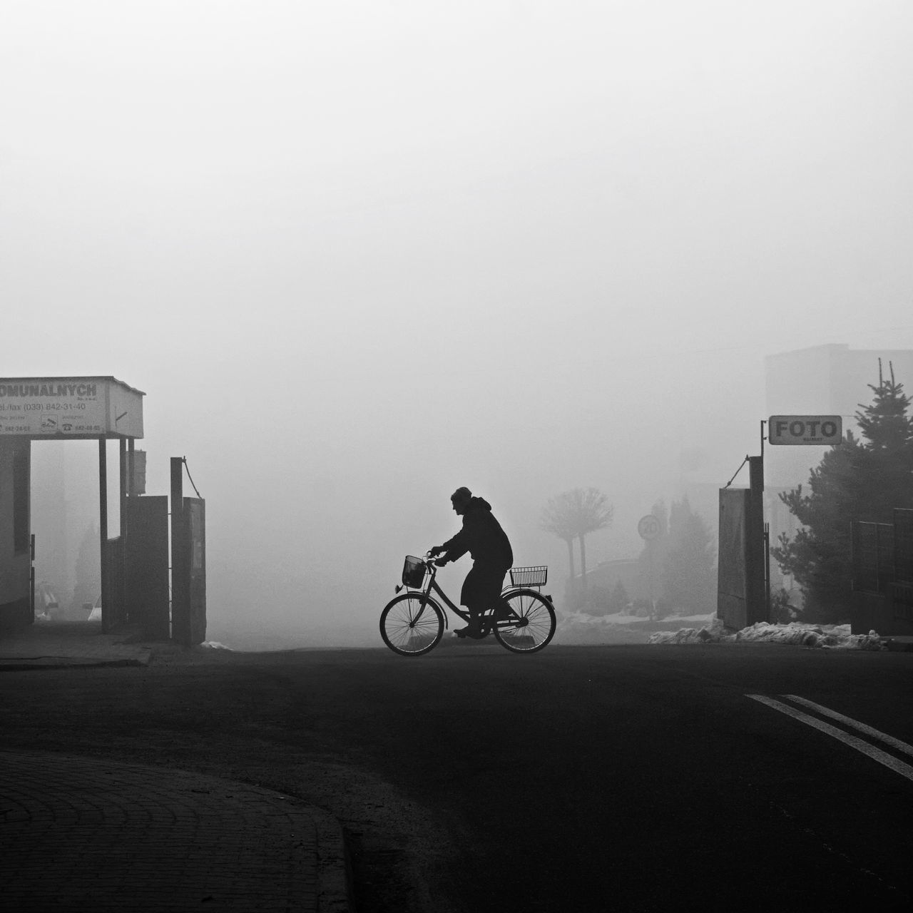 MAN RIDING BICYCLE ON ROAD IN CITY AGAINST SKY
