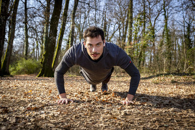 The blue-eyed man is doing push-ups in the woods while listening to music.
