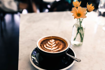 Cup of hot cappucino on marble table background in the black cup. some flowers are closed