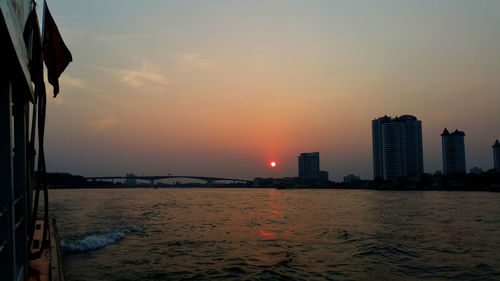 Sea by buildings against sky during sunset