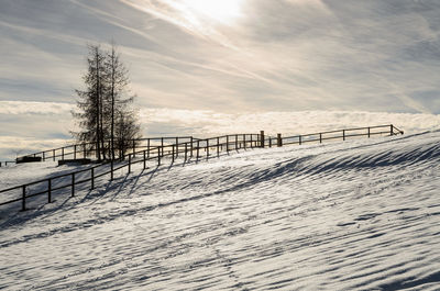 Fence on snow covered land against sky
