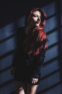 Beautiful young woman looking away while standing against wall