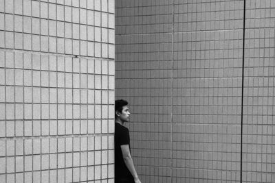 Side view of thoughtful young man looking away while standing by wall