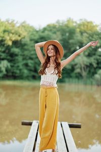 Side view of young woman wearing hat standing against lake