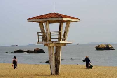 Rear view of men walking by wooden lookout tower at beach