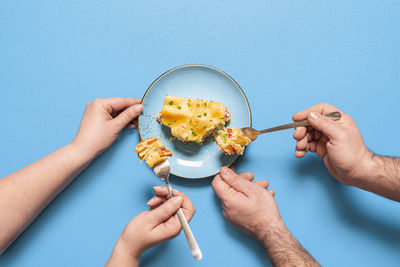 People sharing and eating a slice of lasagna,  on blue background. flat lay with vegetable lasagna.