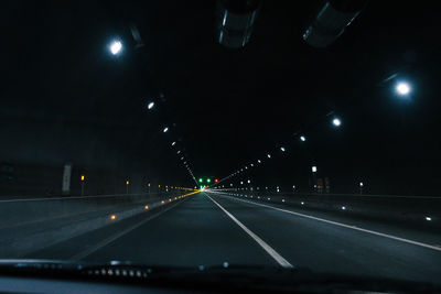 Illuminated road in tunnel seen through car windshield