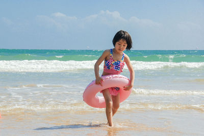 Full length of girl with inflatable ring walking at beach against sky