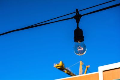 Low angle view of light bulb hanging against clear blue sky