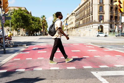 Side view of ethnic male in casual wear crossing asphalt road on sunny day in barcelona