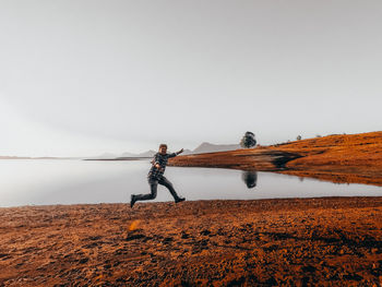 Portrait of happy man jumping at shore against clear sky