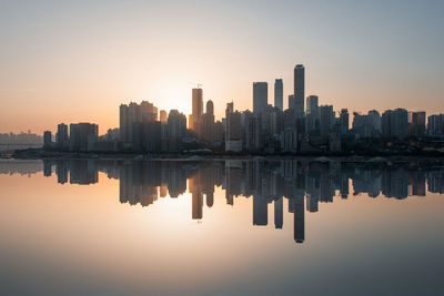 Reflection of buildings in sea against sky during sunset