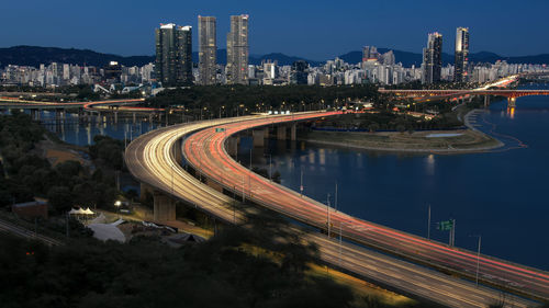 High angle view of light trails on road by buildings against sky at night