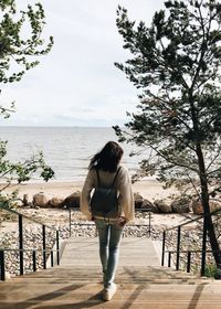 Rear view of woman walking on steps against sea at beach