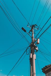 Low angle view of electricity pylon against blue sky