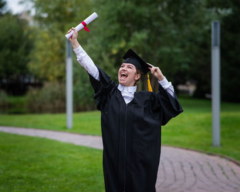 Smiling young woman wearing graduation gown standing on field