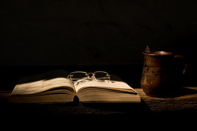 Close-up of metallic jug by eyeglasses on open book in dark